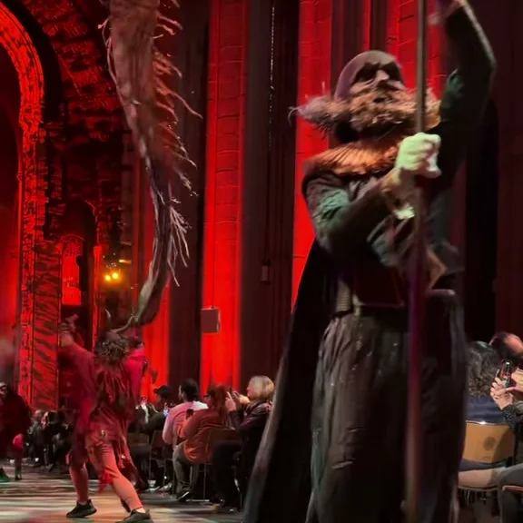 Hooded figure with raised staff mid-procession